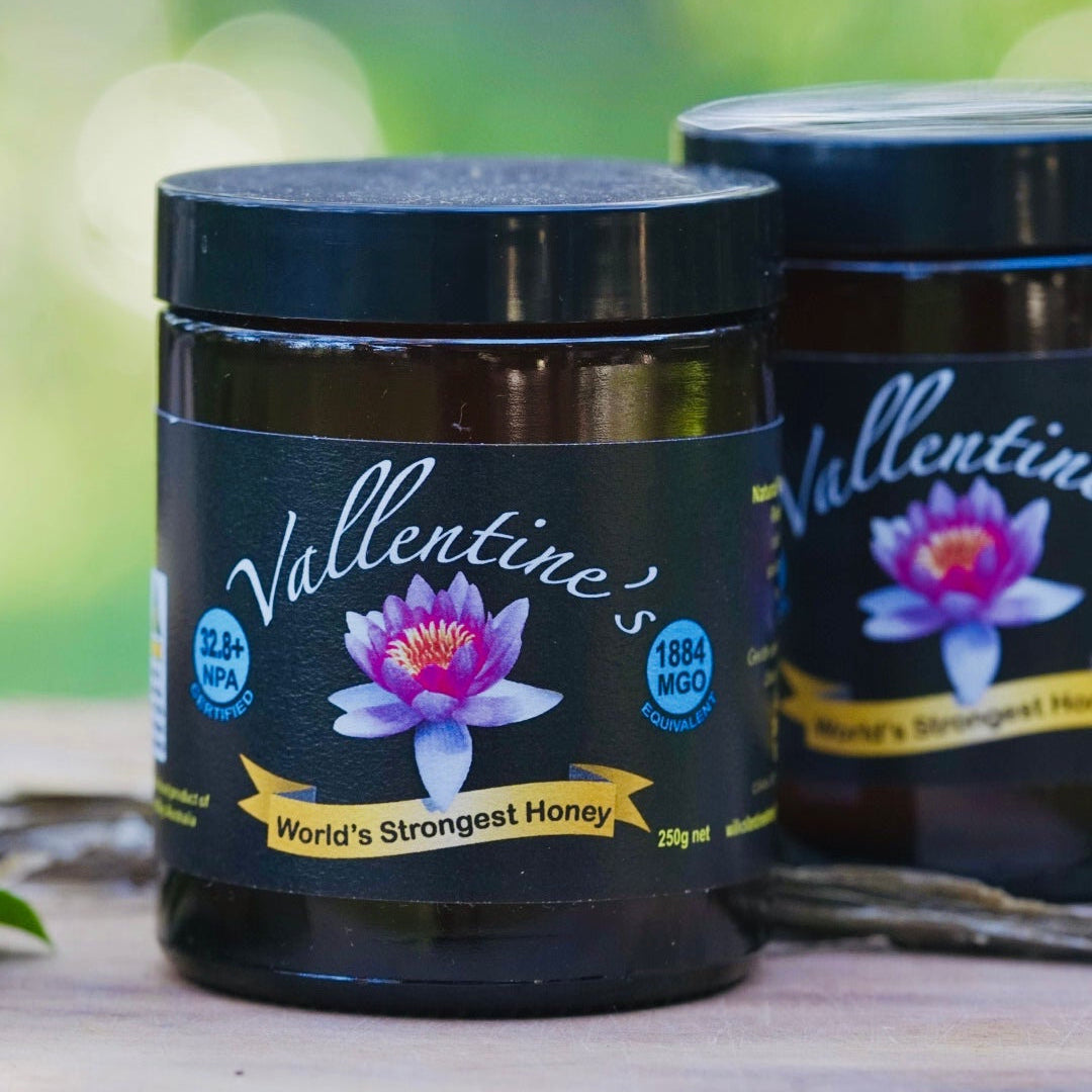 Two jars of Vallentine's honey on a wooden surface with a blurred natural background